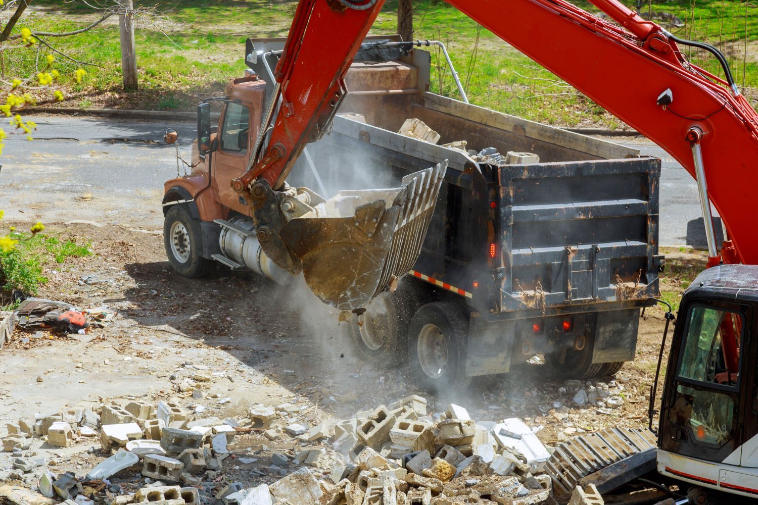 A red excavator is loading dirt into a dump truck.