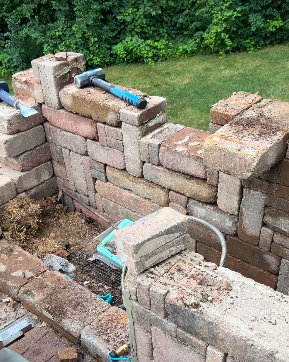 A brick wall is being built on a patio next to a grill.