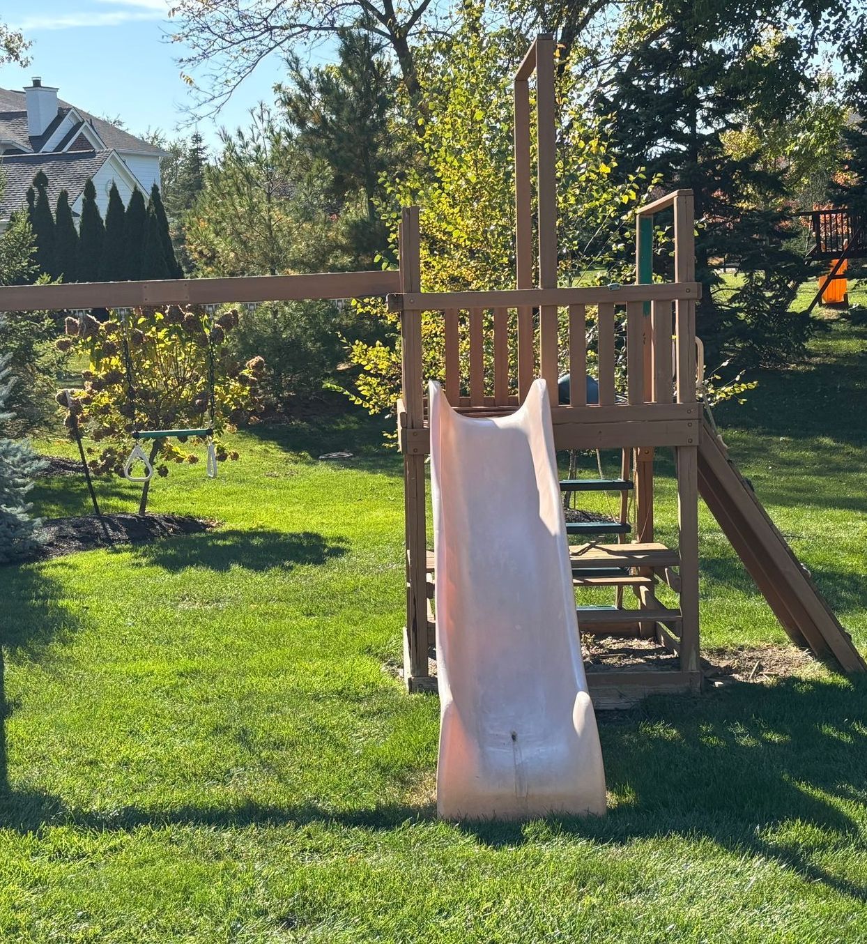 A wooden playground with a slide and swings in the backyard