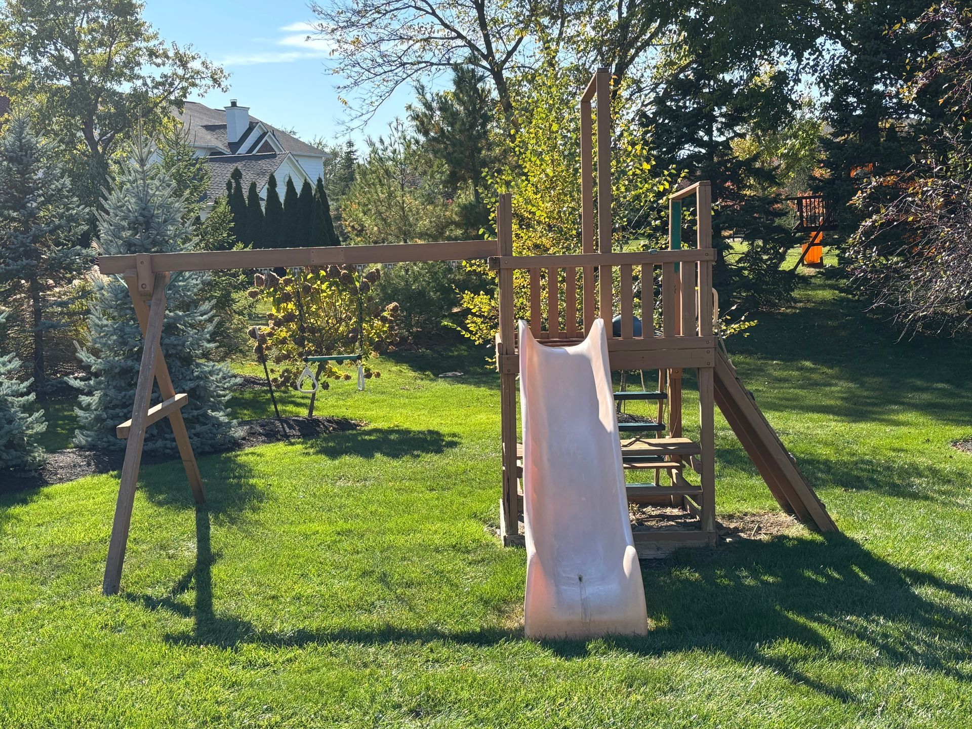 Wooden playground set with swing set, slide, and climbing structure on a grassy lawn.
