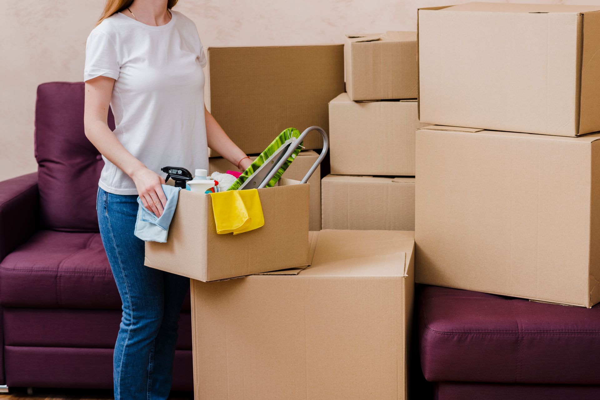 A woman is holding a cardboard box with cleaning supplies in it.