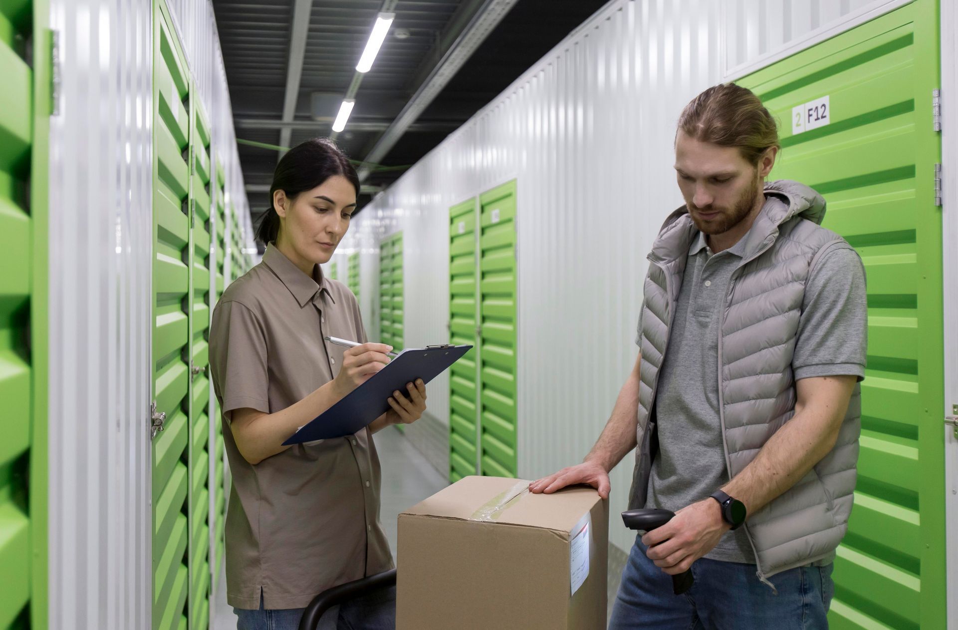 A man is scanning a box in a warehouse while a woman writes on a clipboard.