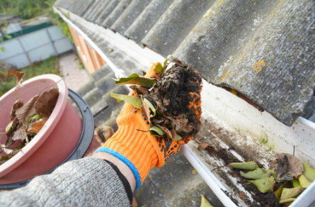 A person wearing orange gloves is cleaning a gutter on a roof. A person wearing orange gloves is cleaning a gutter on a roof.