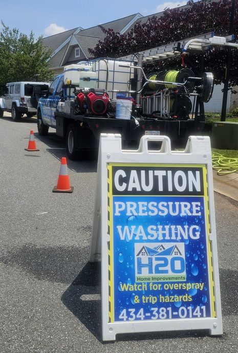 Caution sign for pressure washing ahead, with a service truck and orange cones on a residential street.