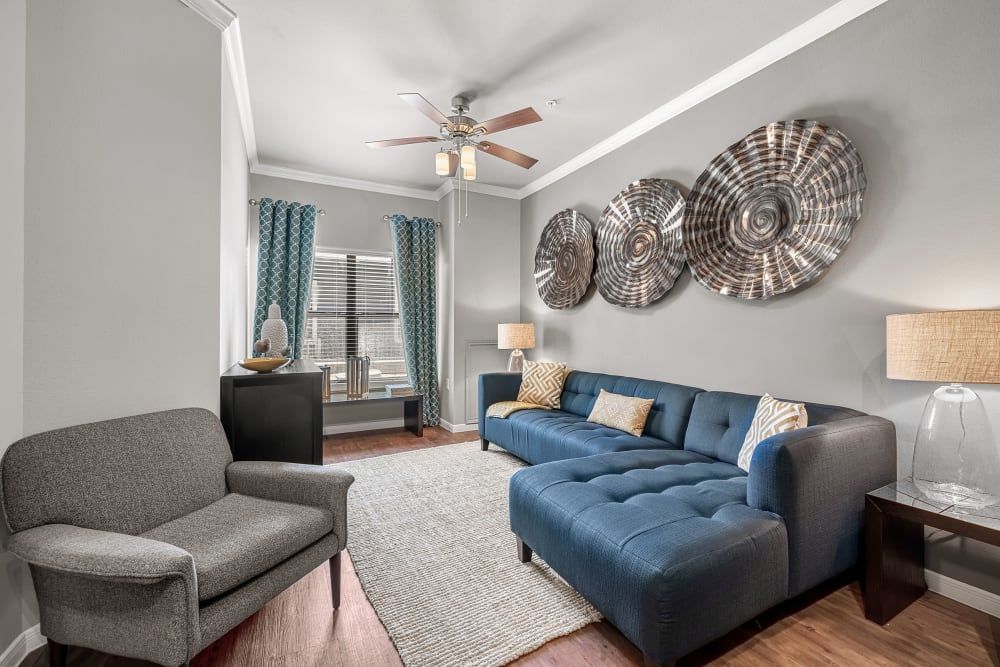 Apartment living room with a blue sectional couch, a chair, and a ceiling fan at Marquis at Texas Street in Dallas, TX.