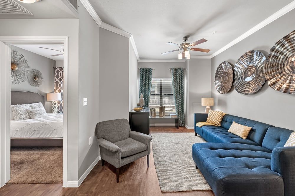 A living room with a blue couch, chair, and ceiling fan at Marquis at Texas Street in Dallas, TX.