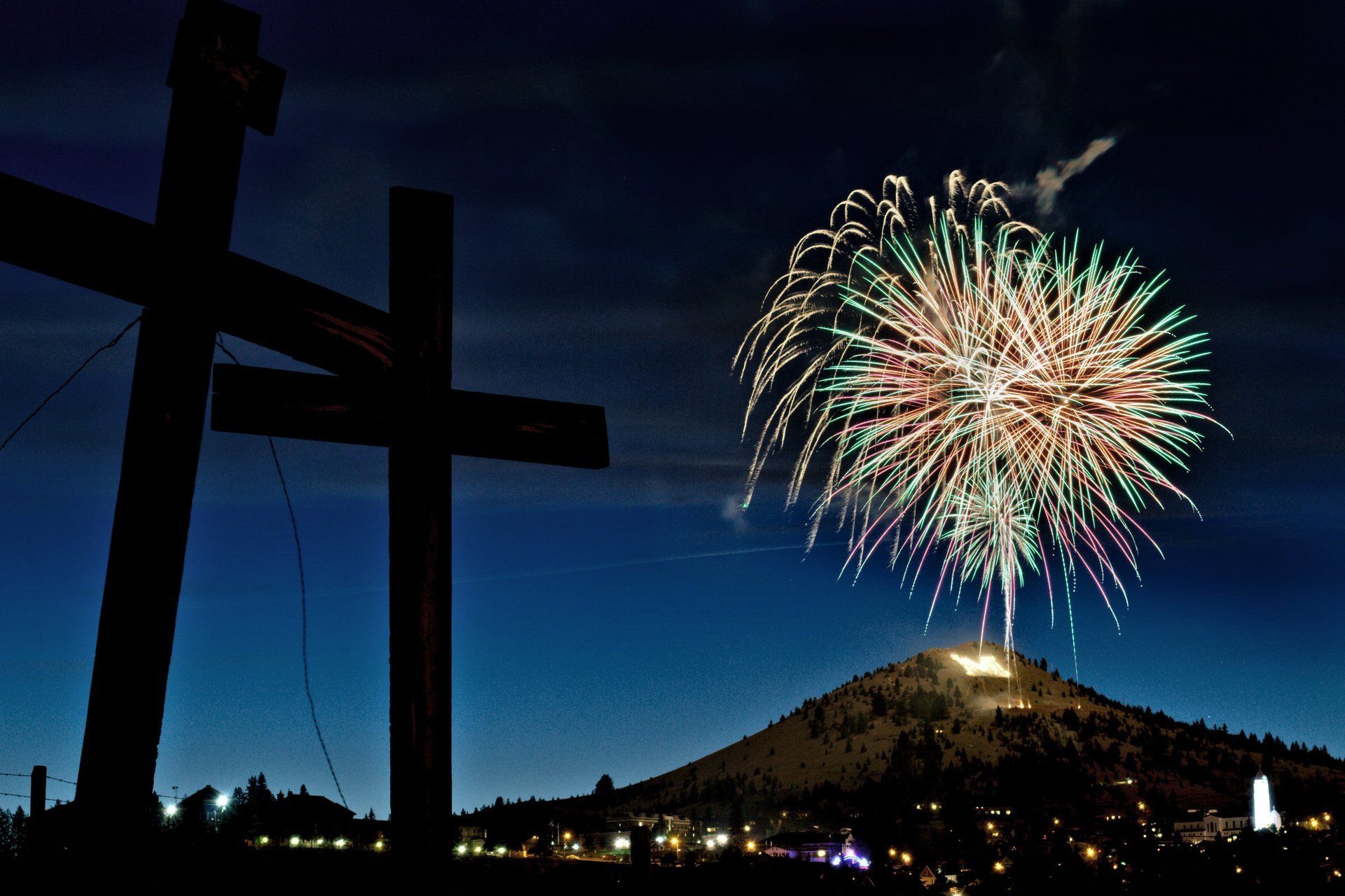 Kimberly Yadao Fireworks exploding in the night sky over  Butte, MT - 2 crosses in silhouetted in the foreground