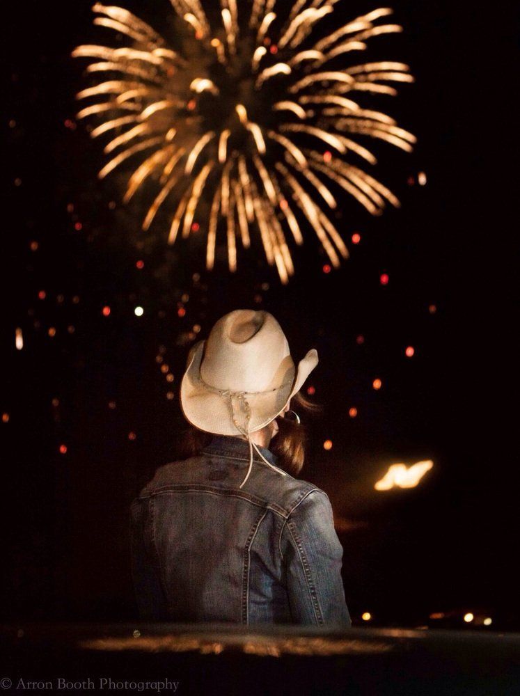 Arron Booth Fireworks exploding in the night sky over  Butte, MT, observed by person with a cowboy hat int he foreground
