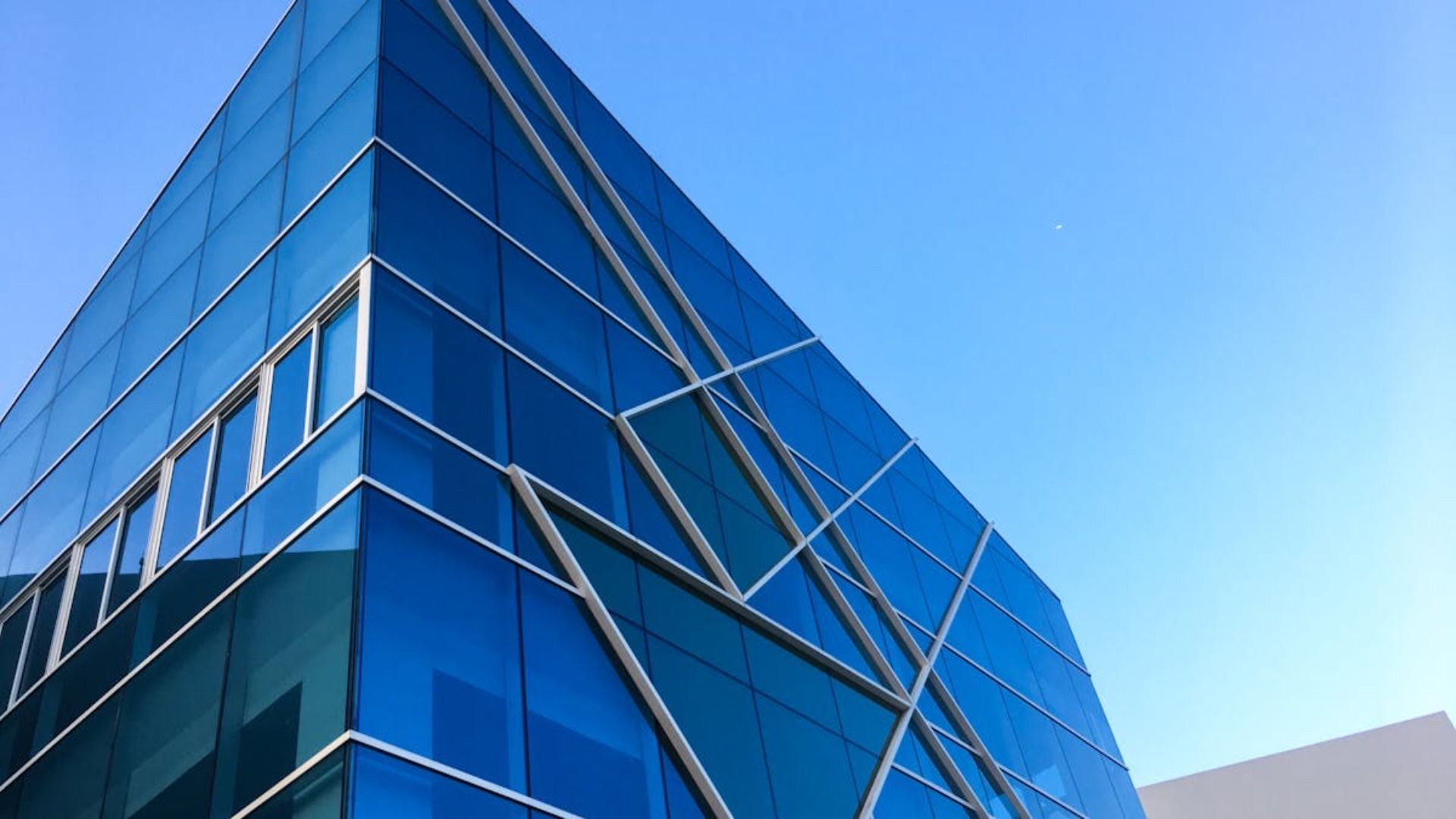 Fachada de cristal azul de un edificio moderno contra un cielo azul despejado.