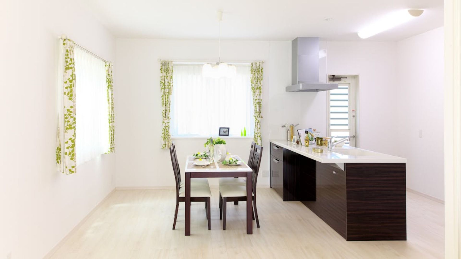 Cocina y comedor luminosos y modernos con una mesa puesta para dos cerca de una ventana con cortinas verdes estampadas.