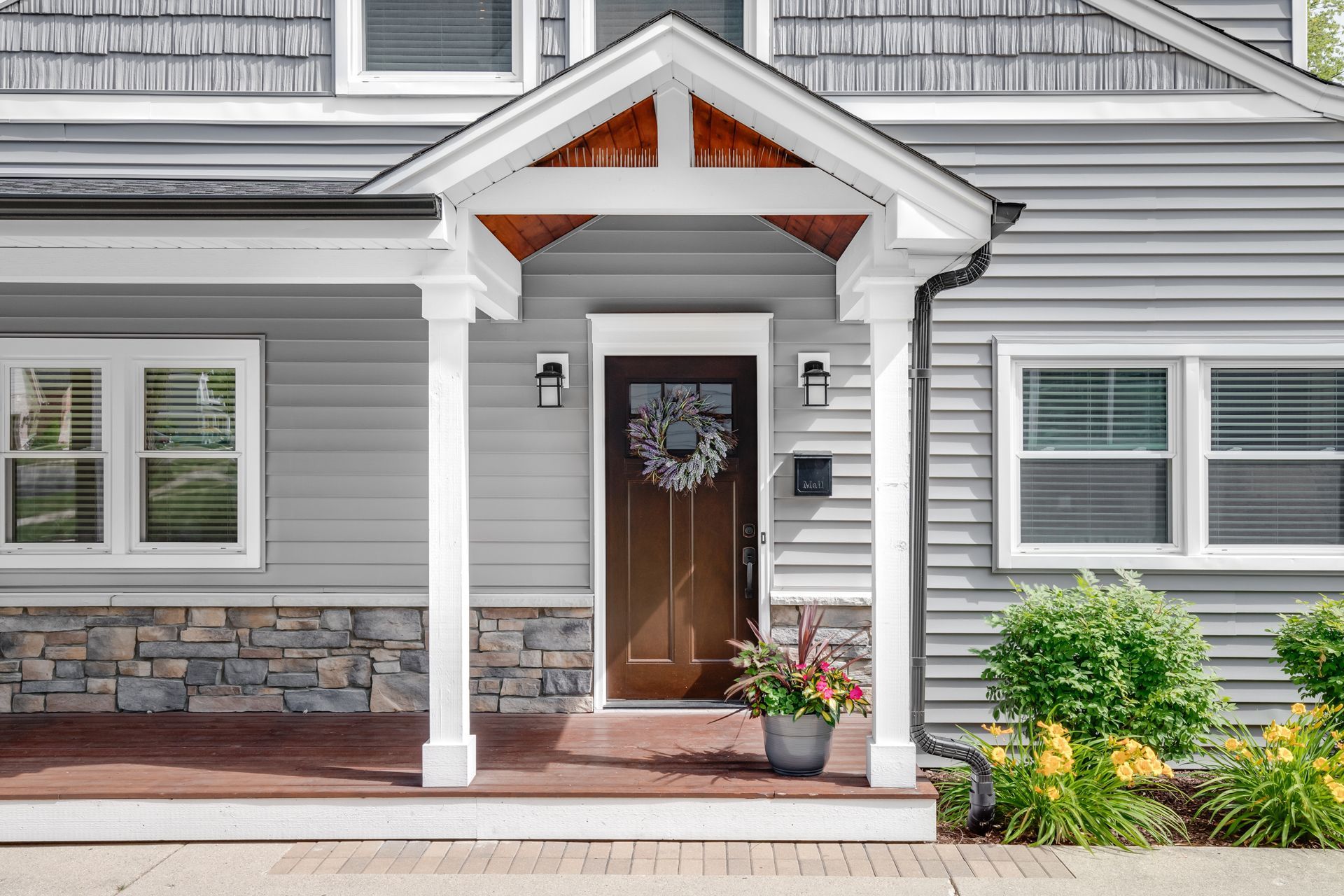 The front of a gray house with a porch and a brown door.