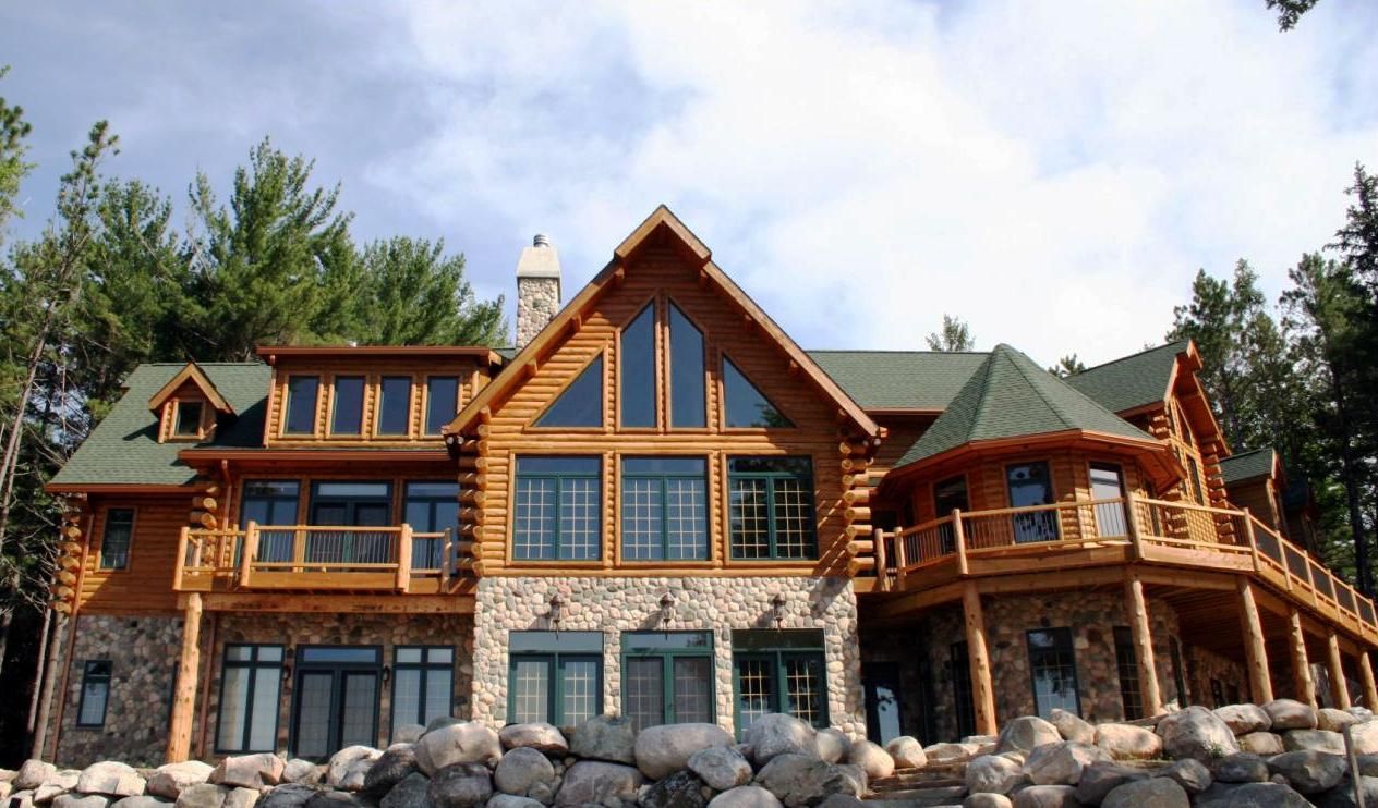 Log cabin home with stone base and green roof on a rocky shoreline.