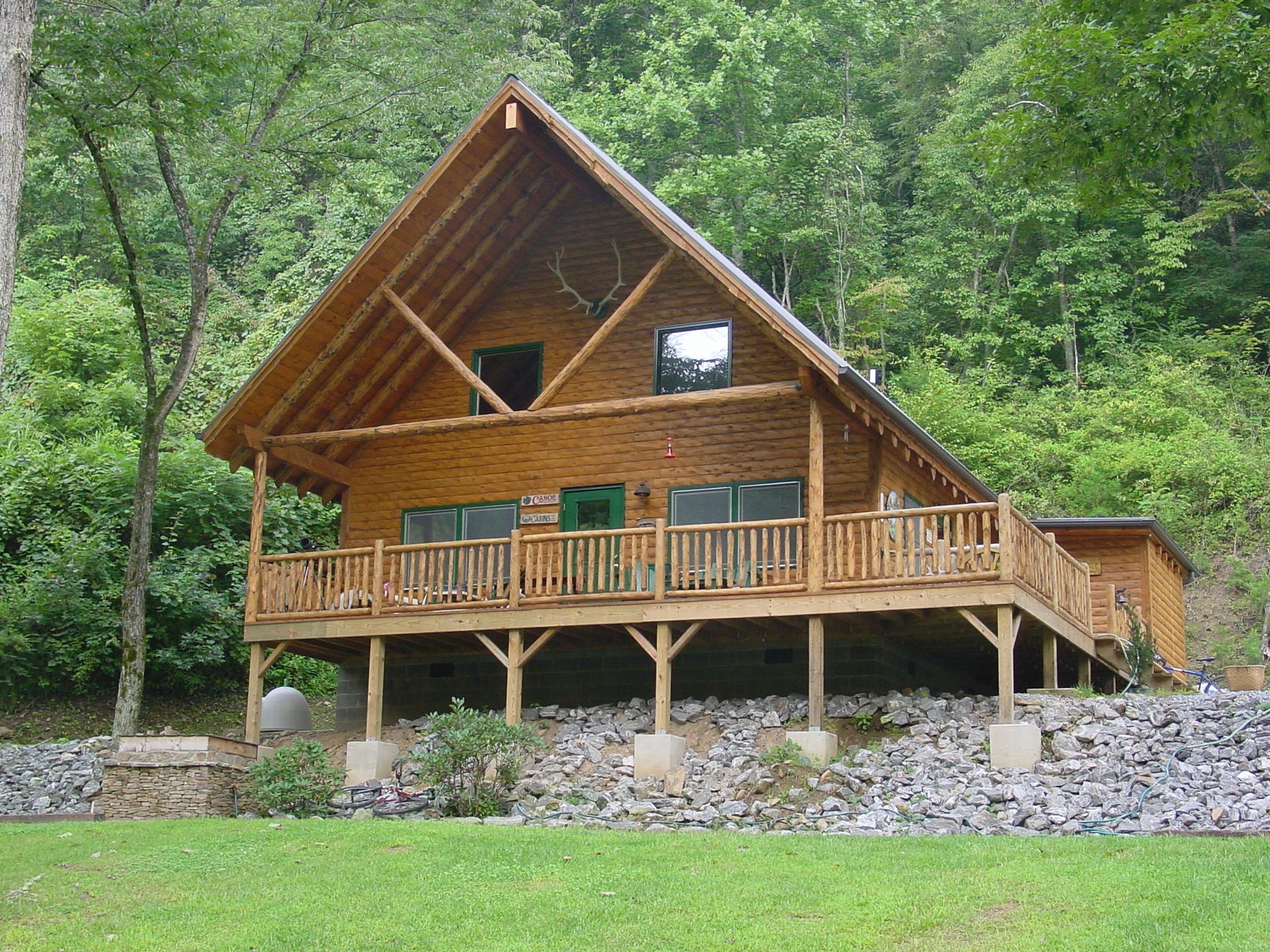 Wooden cabin with a porch and deck in a wooded setting.