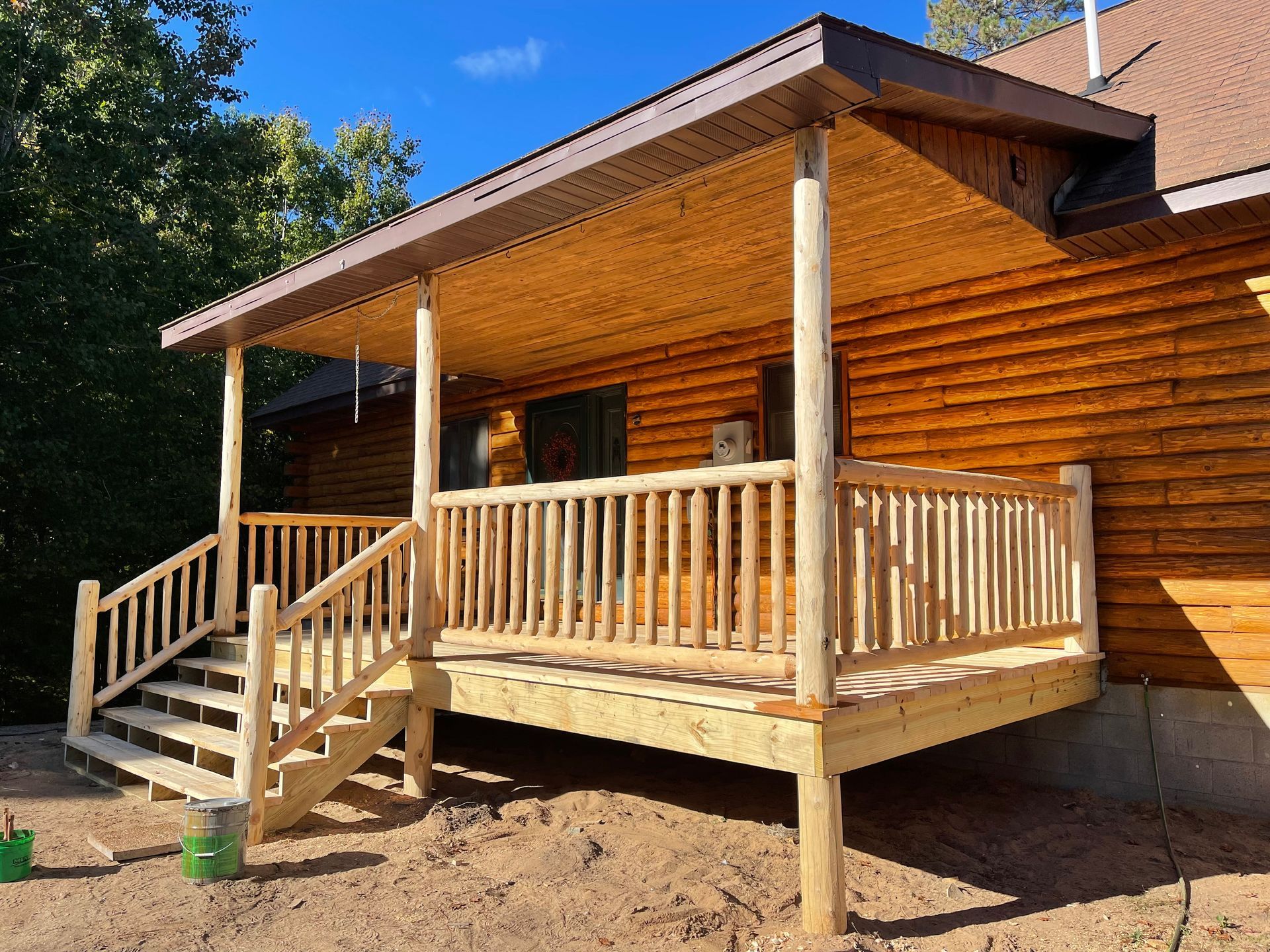 Wooden porch and steps attached to a log cabin, with a tan roof.
