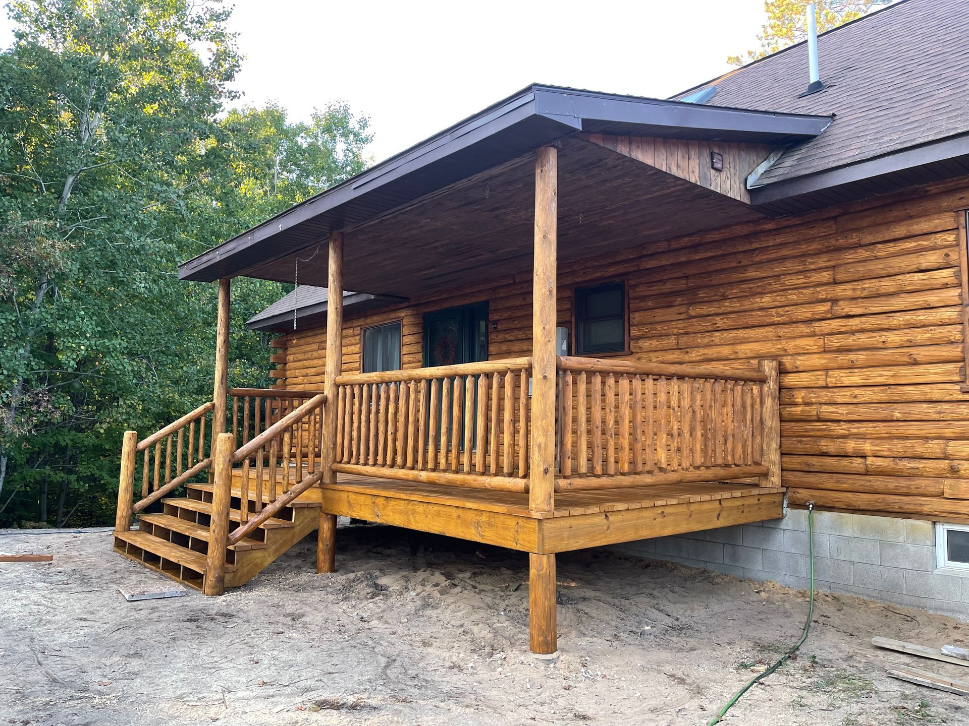 Wooden porch with stairs, railing, and roof on a log cabin-style house.