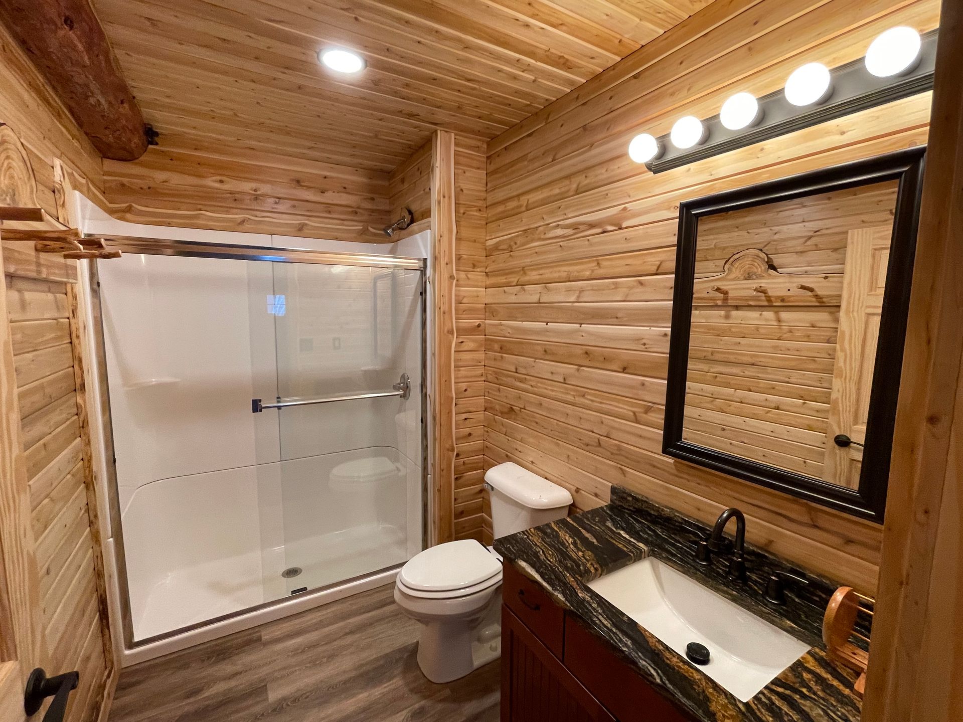 Bathroom with wood paneling, a shower, a toilet, a vanity with a dark countertop and mirror.