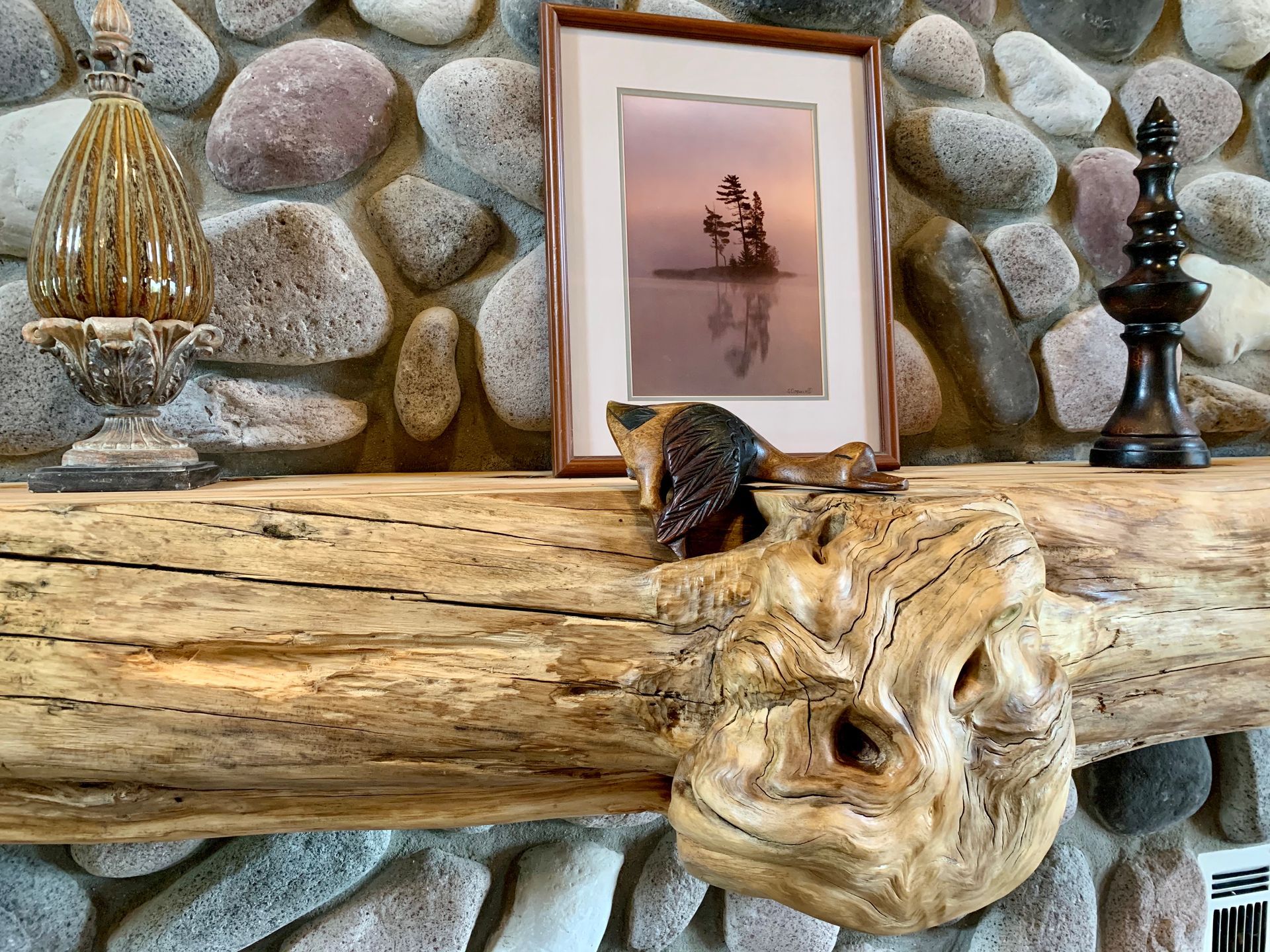 Mantle with art and carved wood. Stone wall backdrop.