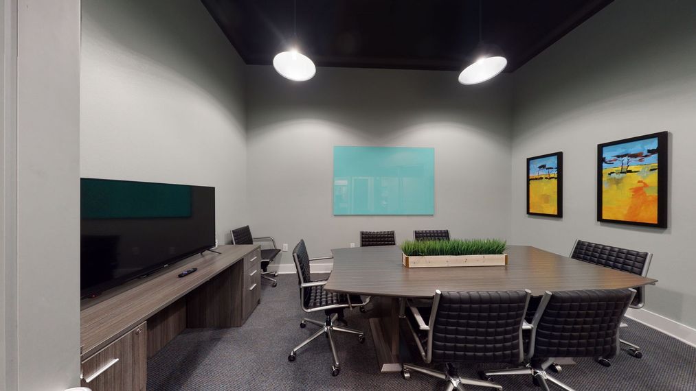 A conference room with a long table and chairs and a television.