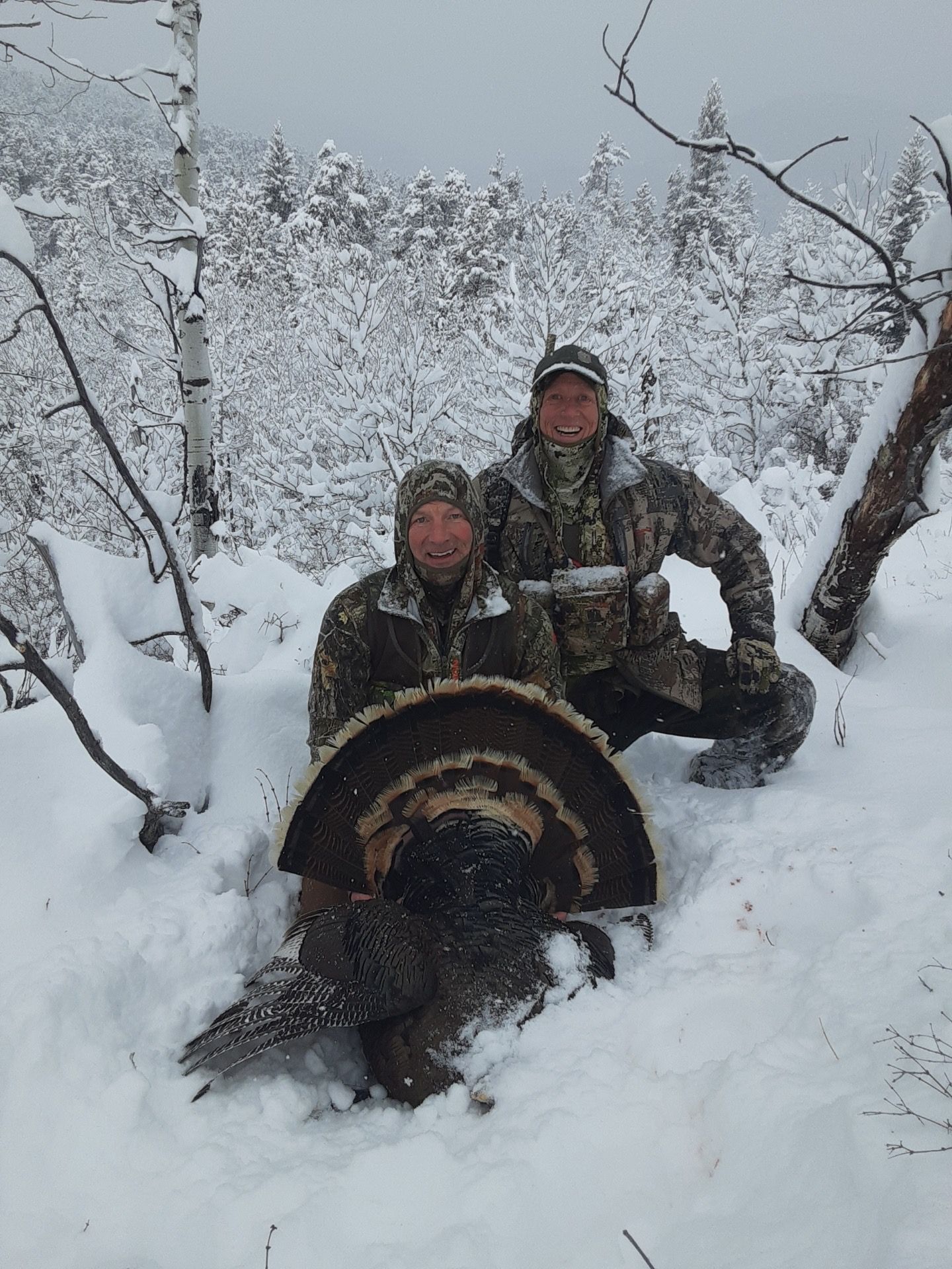Two men kneeling behind a dead turkey in the snow