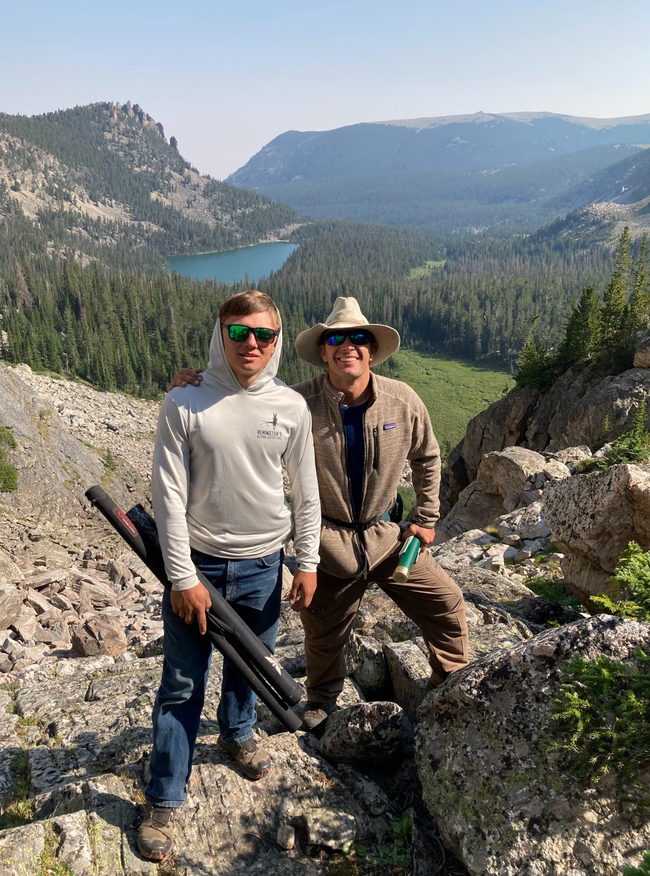Two men are standing on top of a mountain holding fishing rods.