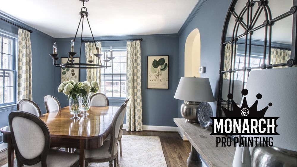 A dining room with blue walls and a monarch pro painting logo