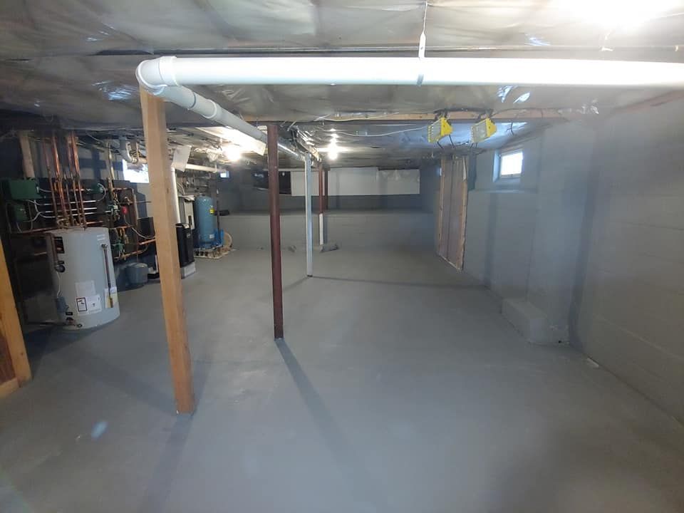 An empty basement with a water heater and pipes.