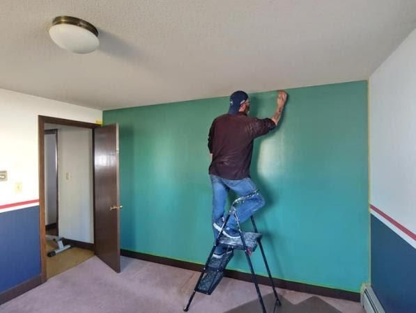A man standing on a ladder painting a green wall