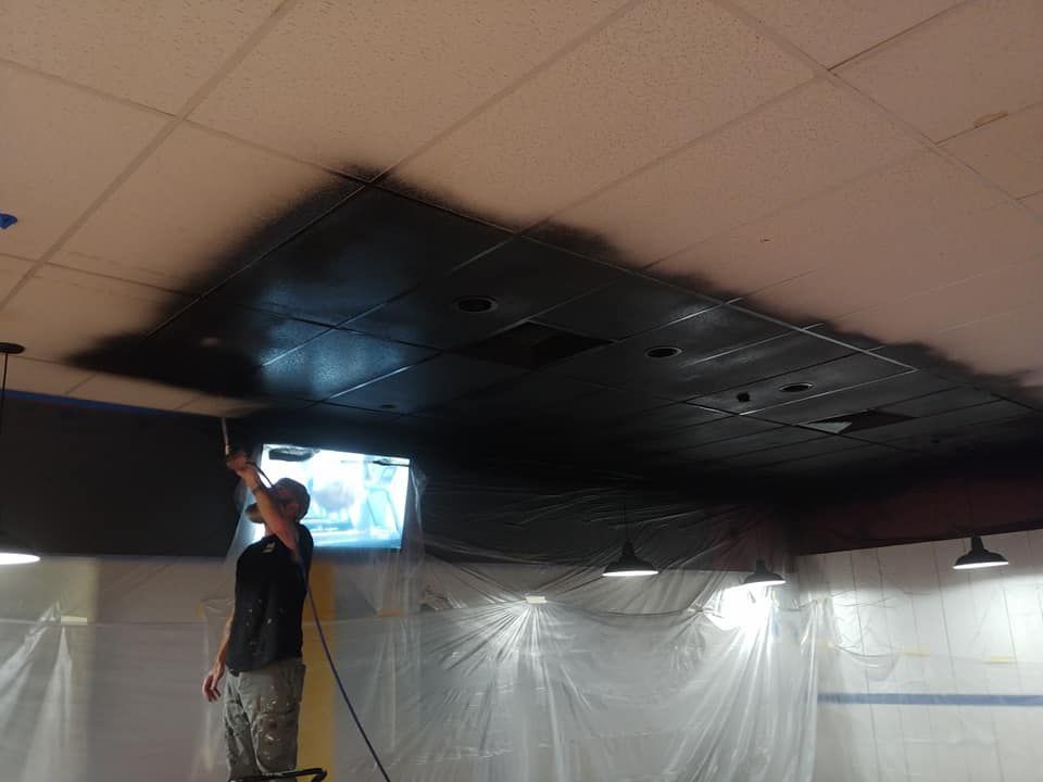 A man is painting a ceiling with black paint