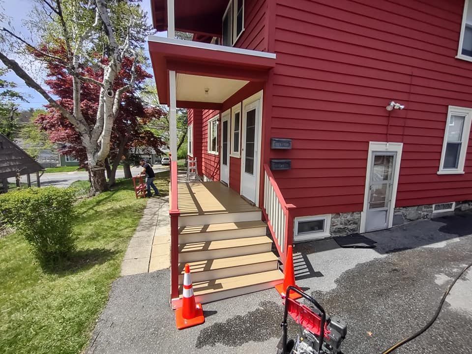 A red house with a porch and stairs is sitting on the side of the road.
