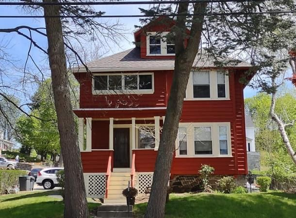 A red house is surrounded by trees on a sunny day