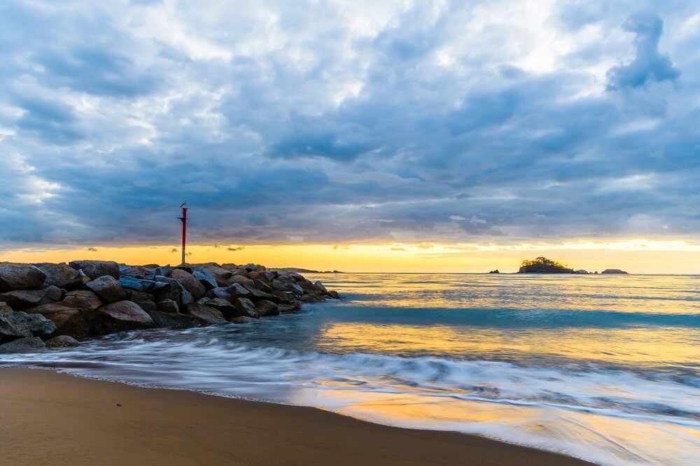 A Beach With Waves Crashing Against A Rock Wall At Sunset — Ballina Demolitions In Ocean Shores, NSW