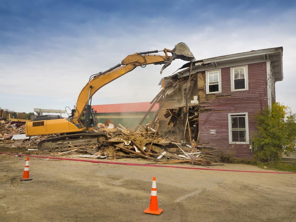 A Yellow Excavator Is Demolishing A Purple House — Ballina Demolitions In Byron Bay, NSW