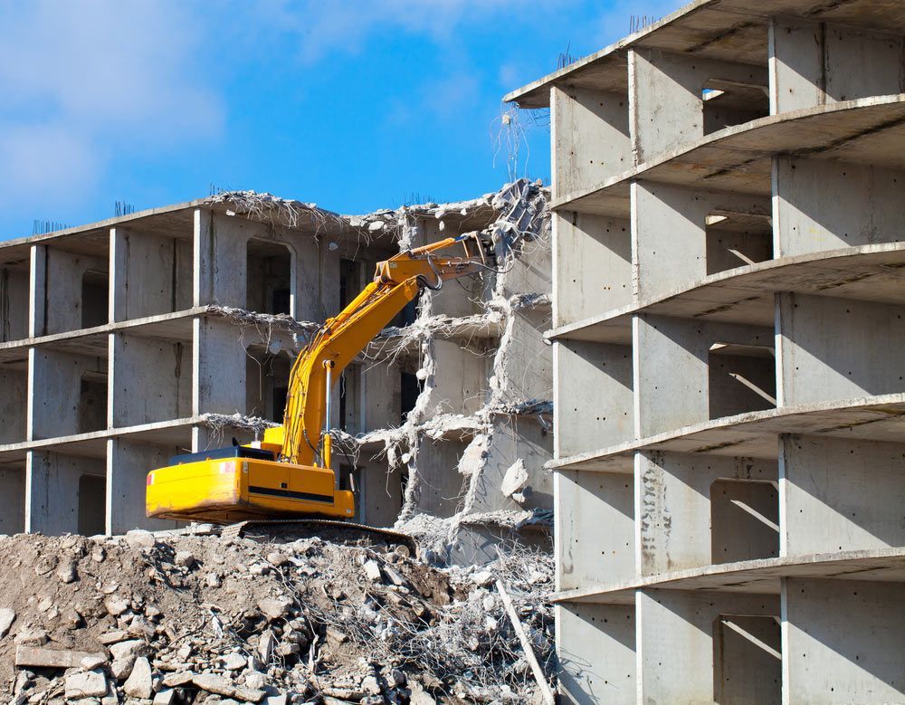 A Yellow Excavator Is Demolishing A Concrete Building — Ballina Demolitions In Ballina, NSW