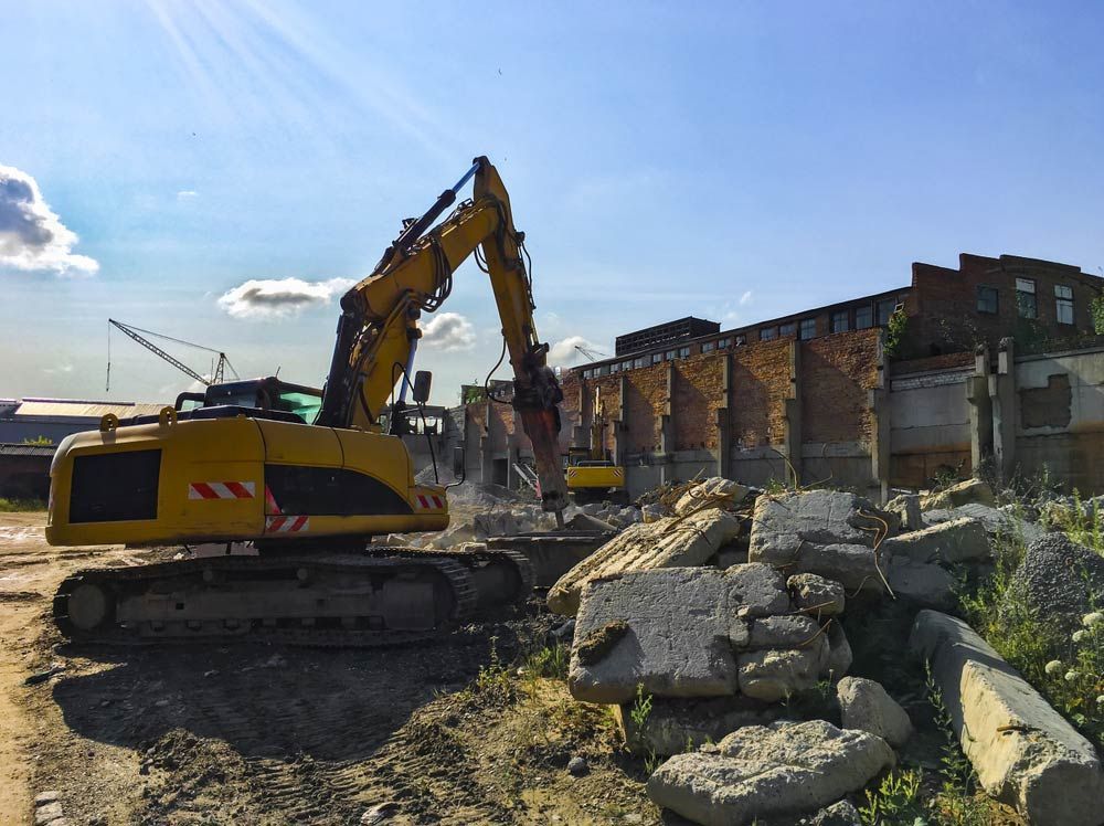 A Large Yellow Excavator Is Demolishing A Building On A Construction Site — Ballina Demolitions In Grafton, NSW