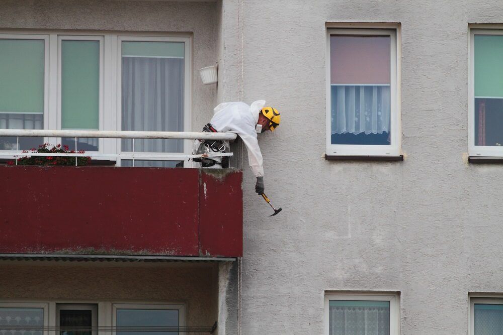A Man Is Standing On A Balcony Of A Building Holding A Hammer — Ballina Demolitions In Casino, NSW