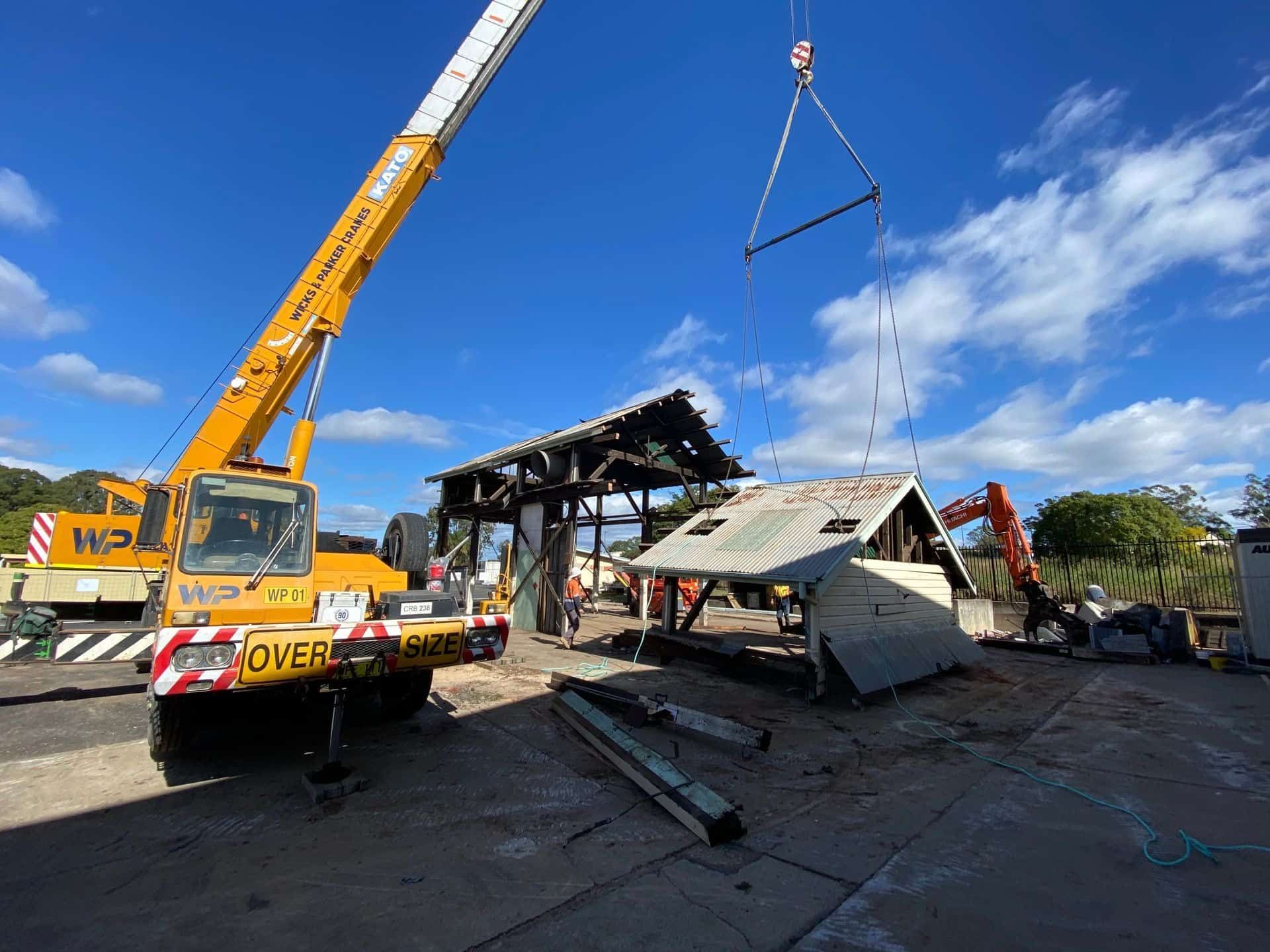 A Yellow Crane Is Lifting A Building In A Parking Lot — Ballina Demolitions In East Wardell, NSW