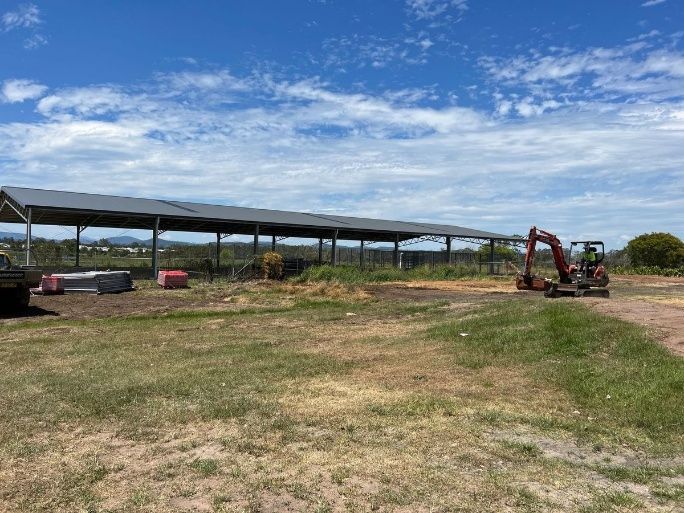A Red Excavator Is Sitting In A Field Next To A Building Under Construction — Ballina Demolitions In East Wardell, NSW