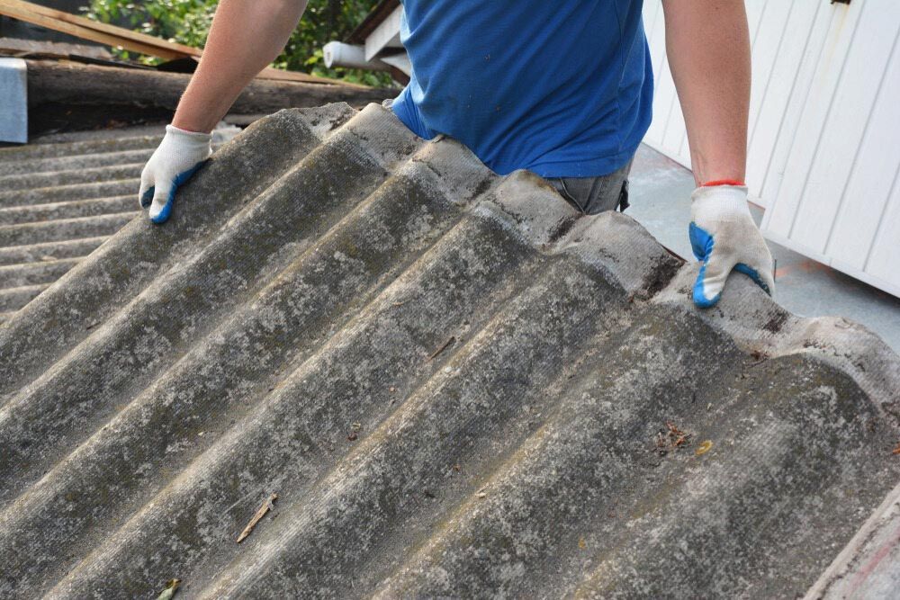 A Man Is Standing On Top Of A Roof Holding A Piece Of Asbestos — Ballina Demolitions In Grafton, NSW