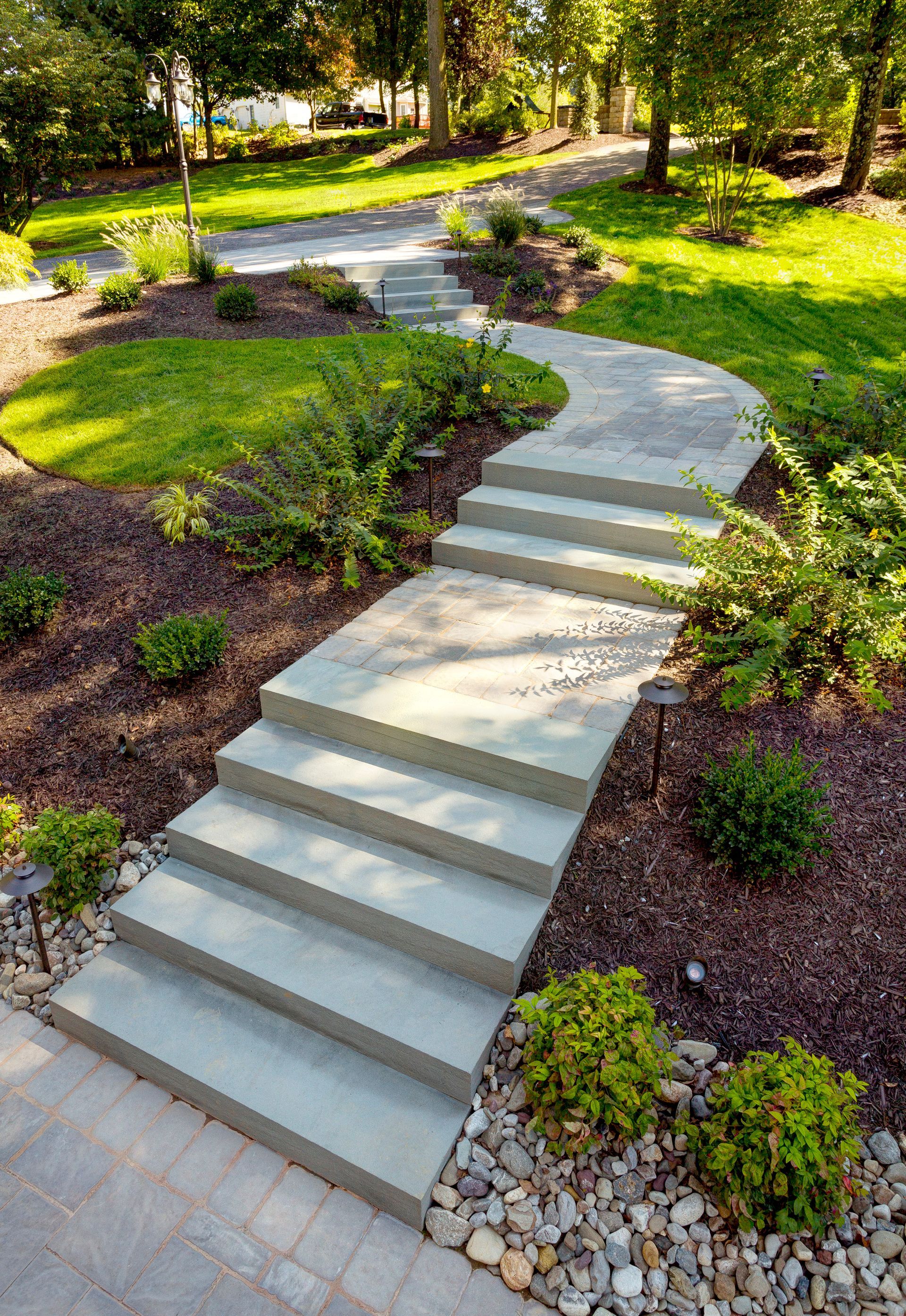 A concrete walkway with stairs leading up to a lush green yard.