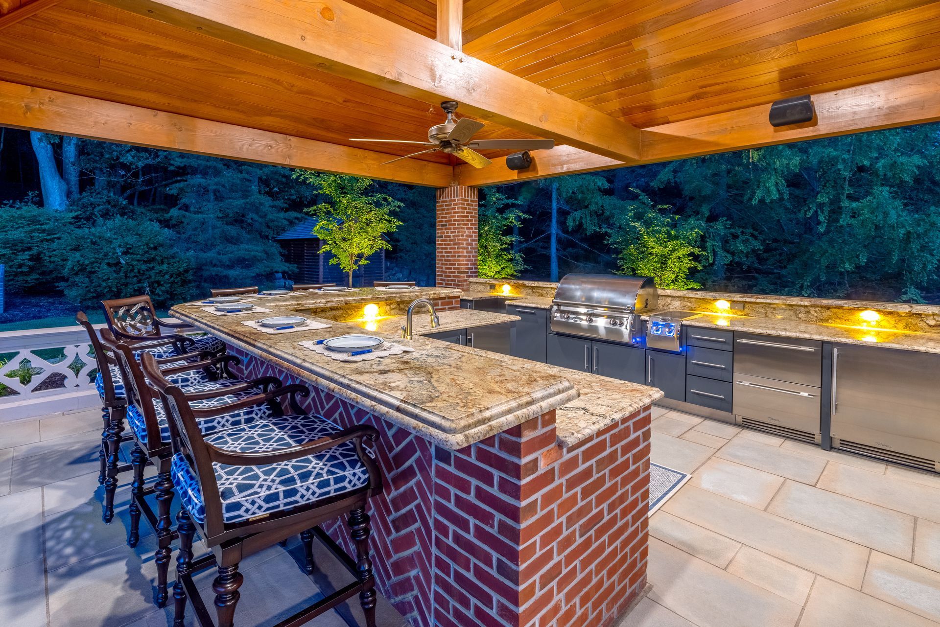 A large outdoor kitchen with a brick counter top and stainless steel appliances.