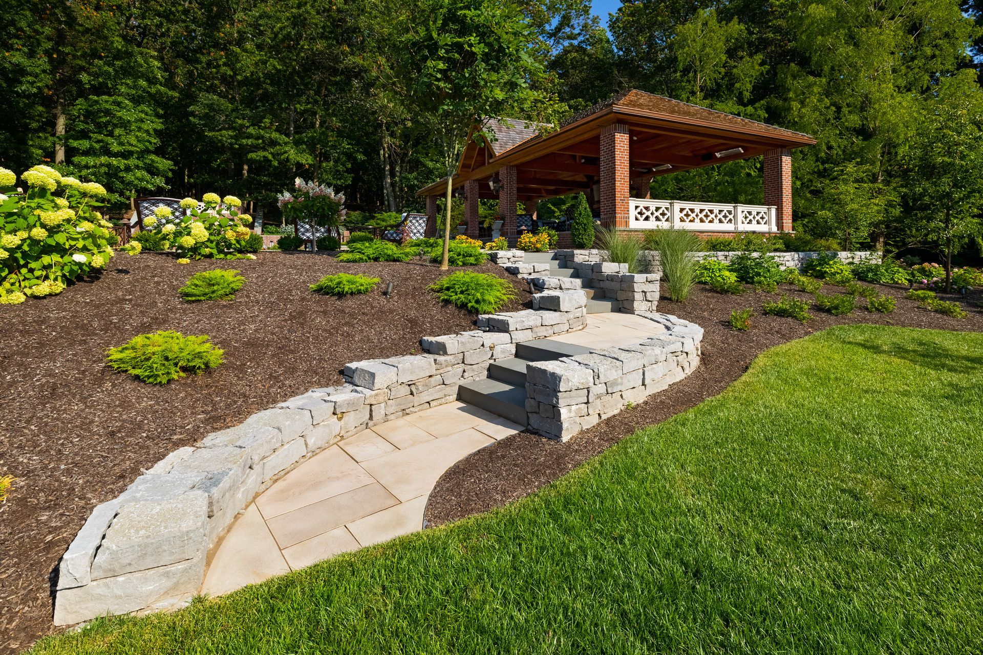 A stone walkway leading to a gazebo in a lush green garden.