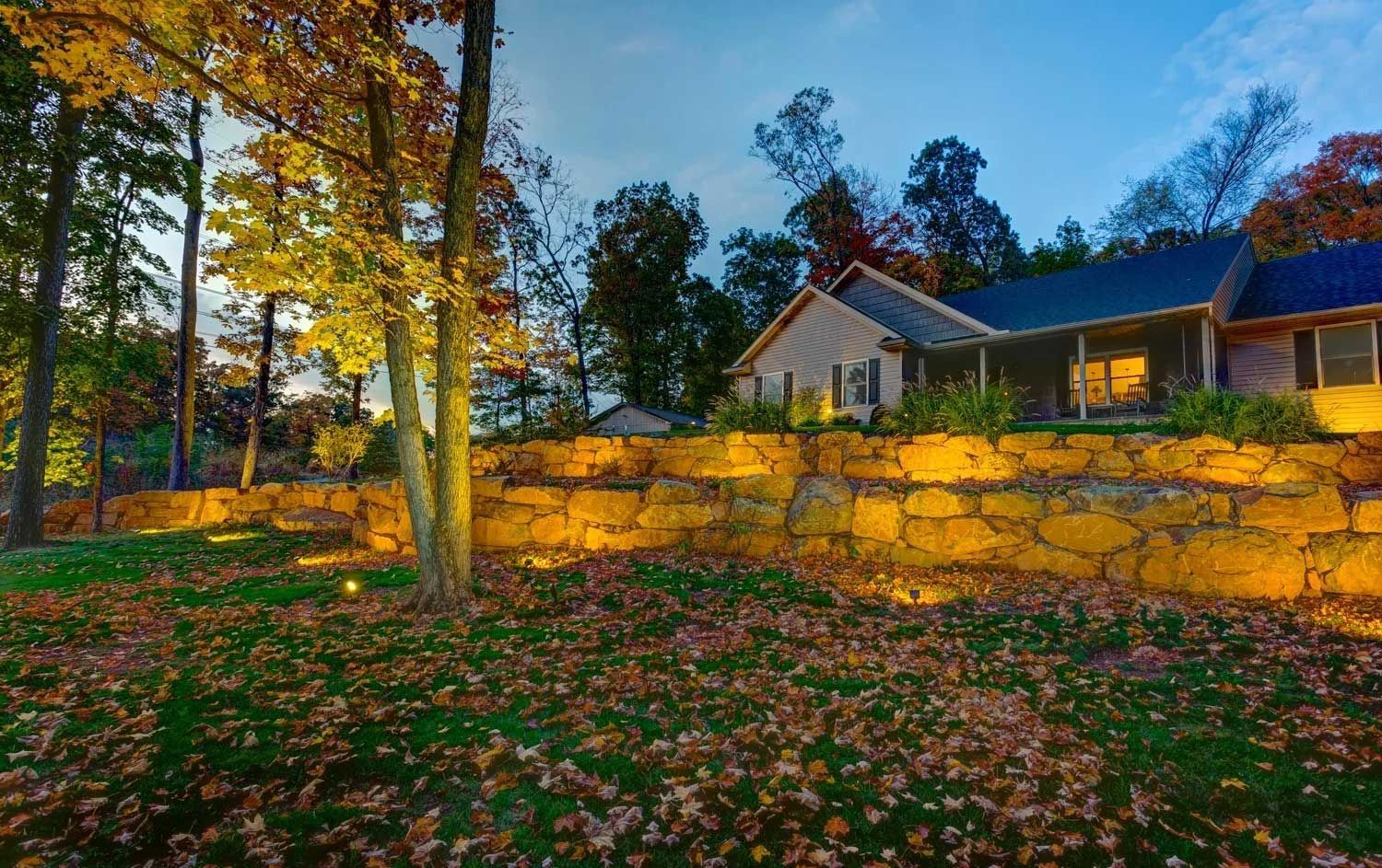 A house with a stone wall in front of it surrounded by trees and leaves.