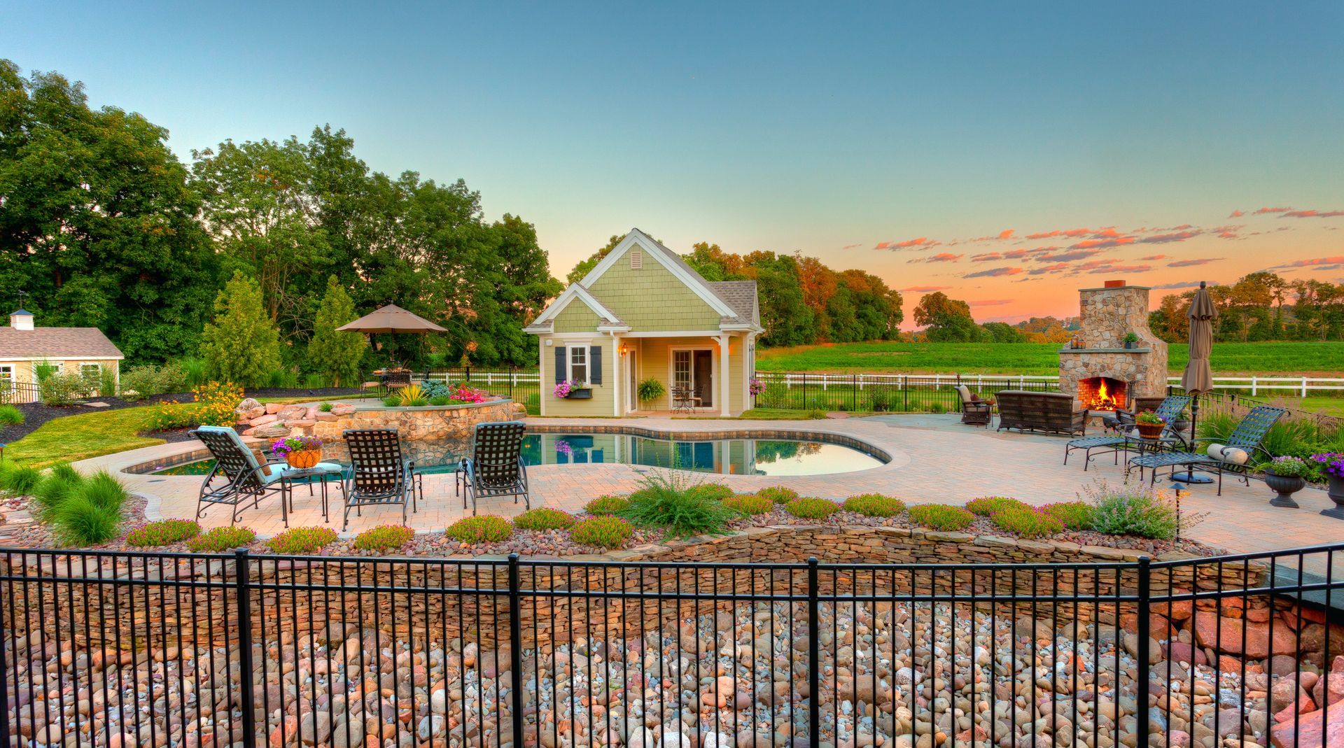 A fence surrounds a large backyard with a swimming pool and a fireplace.