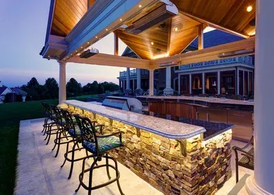 A large outdoor kitchen with a bar and chairs under a canopy.