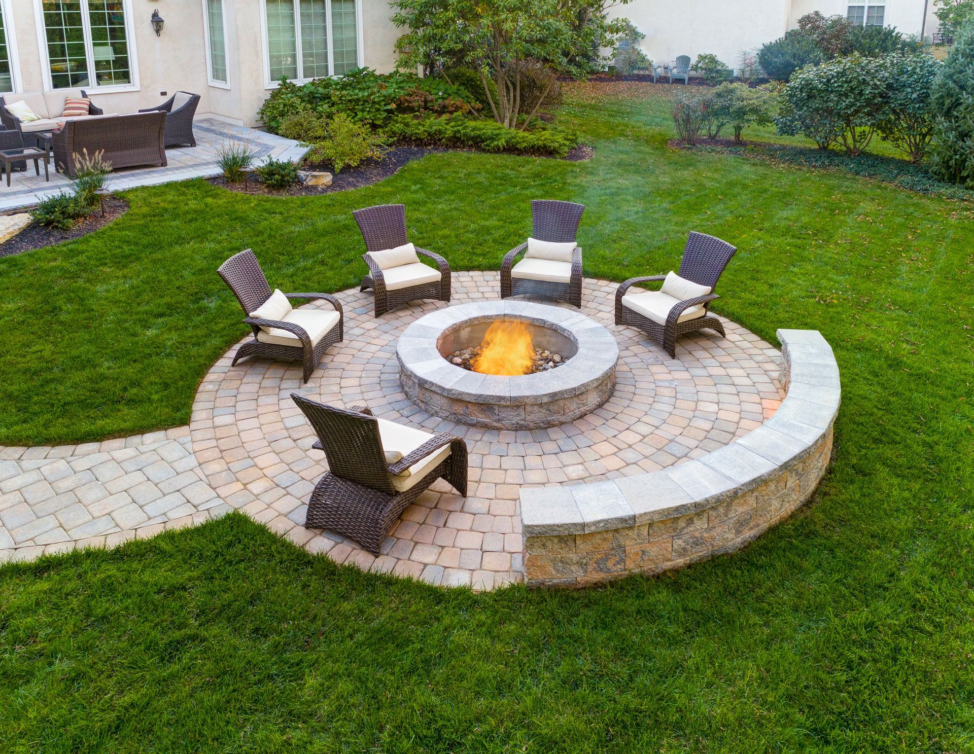 A fire pit in the middle of a lush green lawn with chairs around it.