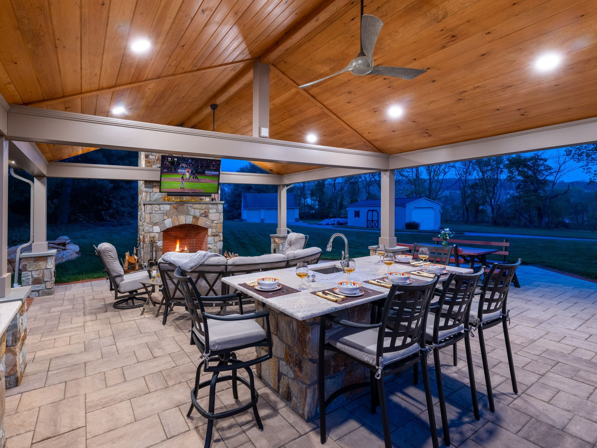 A patio with a table , chairs , a fireplace and a ceiling fan.