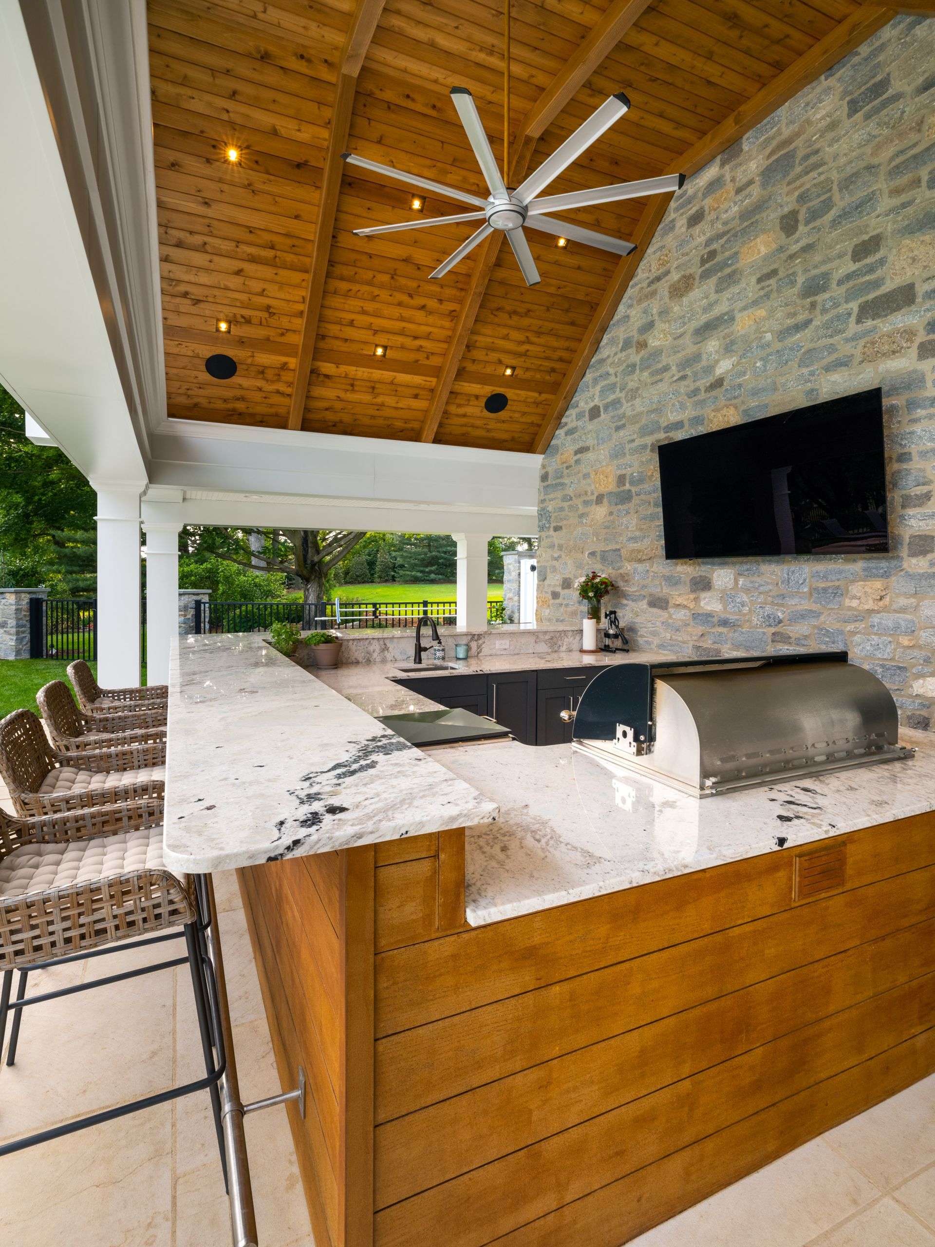 An outdoor kitchen with a ceiling fan and a flat screen tv.