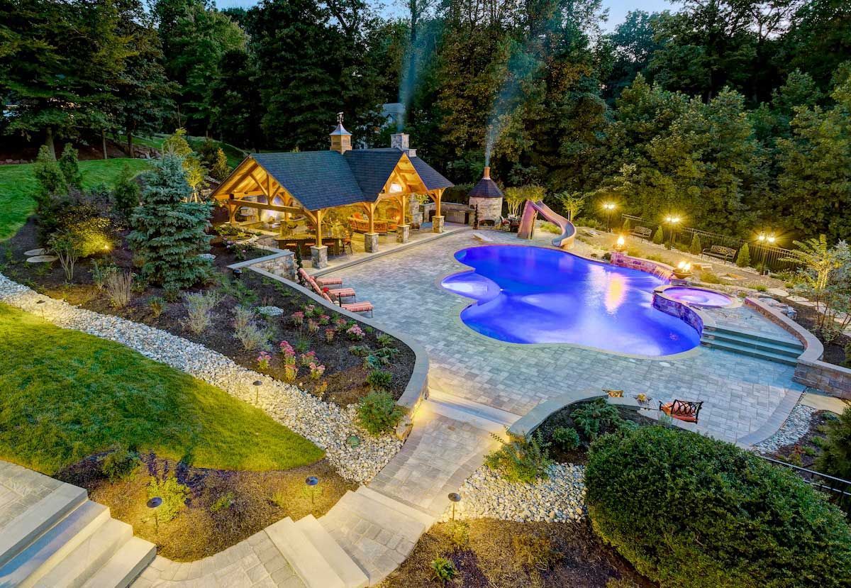 An aerial view of a large swimming pool with a log cabin in the background.