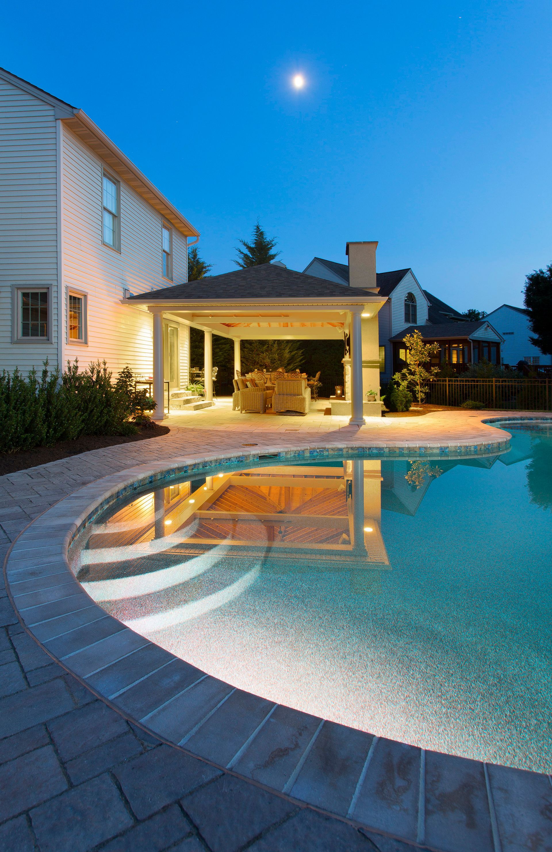 A large swimming pool in front of a house at night