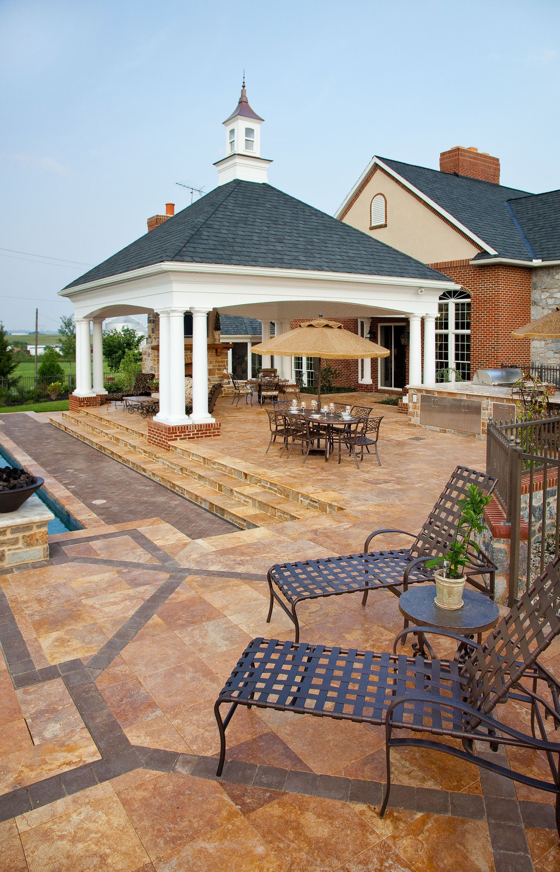 A gazebo with umbrellas and chairs in front of a house.